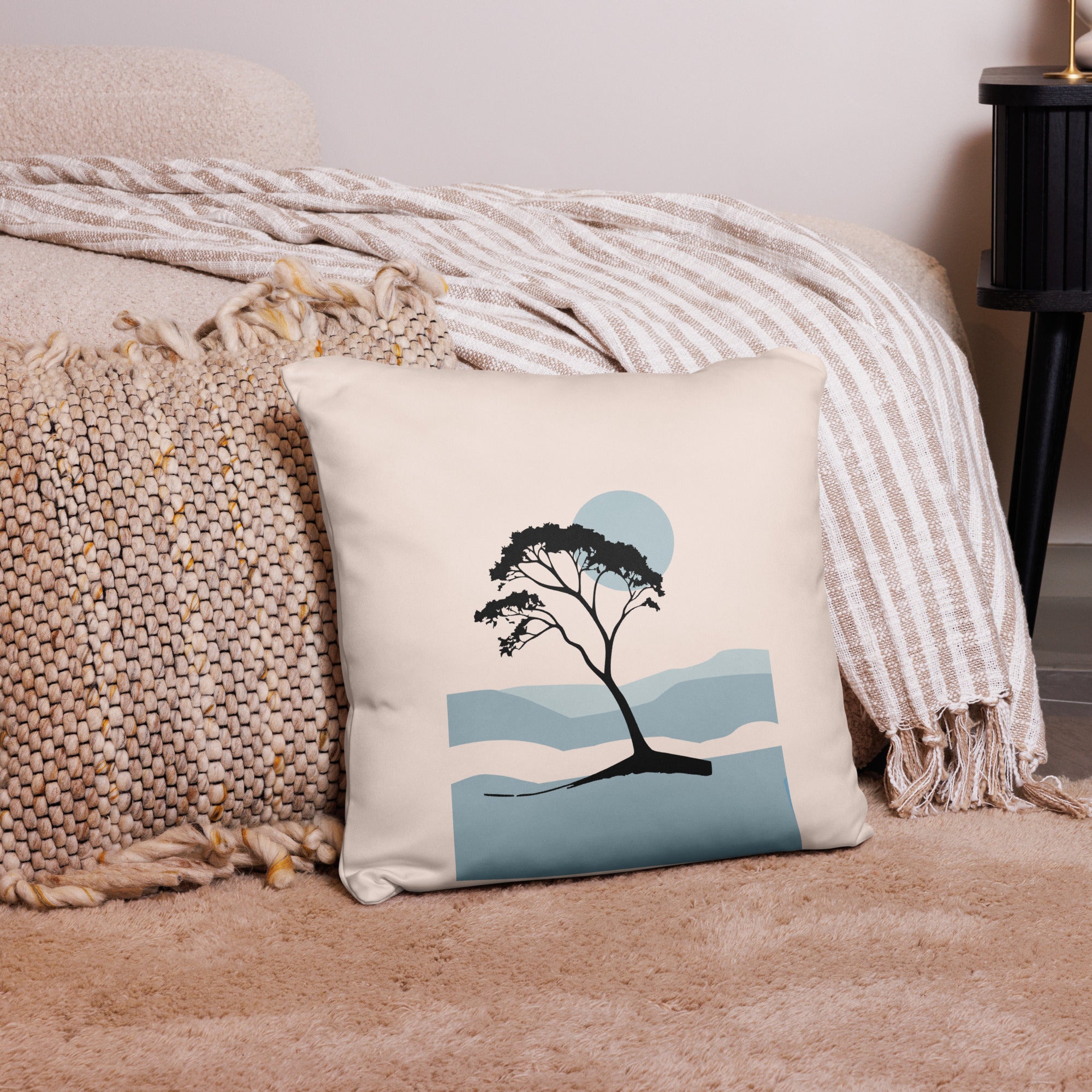 Beiges Dekokissen mit minimalistischer Baum-Illustration „Soft Horizon“ in Blau- und Schwarztönen, dekorativ auf Sofa platziert